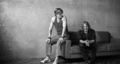 A black and white photo of two men sitting on a couch and smiling to themselves.