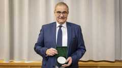 Ein Mann im Anzug hält eine Schatulle mit einer weißen Medaille in den Händen.