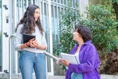 dos estudiantes conversan animadamente frente a su facultad
