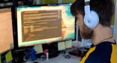 Bearded developer wearing white headphones working at dual-monitor setup with dark mode screens and sticky notes