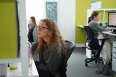 Woman with curly hair and glasses working at office desk, wearing grey sweatshirt