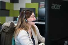 Smiling woman in white cardigan wearing Sennheiser headset while viewing Acer monitor