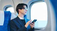 列車の座席に座り、安心した表情でスマートフォンを触る男性。