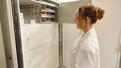 Woman in lab coat checking specimen samples in freezer container