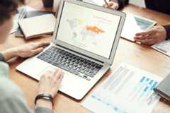 kuva pöydästä jossa työskennellään, etualalla tietokone joss anäkyy maailman kartta ja liiketoiminta-sanastoa.