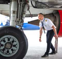 Nolinor-Photo-Pilote A pilot inspects the landing gear of an aircraft, focusing on the wheel and undercarriage components.