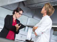 Female inspector takes notes during a restaurant kitchen inspection