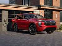 2026 Nissan Rogue PHEV 3/4 front view parked next to a house in the hills plugged into the home charger