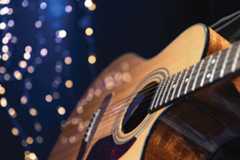 An acoustic guitar on a dark blue background with white twinkle lights