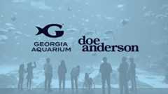 People looking into an aquarium tank filled with fish and Georgia Aquarium and Doe Anderson logos in the center