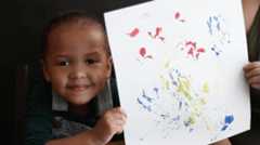 A young child creates art by painting with leaves
