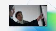 Engineer pointing at code displayed on a large monitor in an office environment.