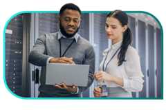 Two professionals wearing company lanyards stand in a data center and work from a laptop.