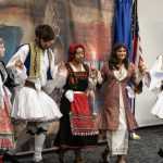 Greek dancers perform in front of a recreation of Rip Kastaris' mural "Kyklos – Circle of Glory"