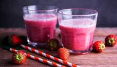 close up of two strawberry smoothies surrounded by red and white striped straws and fresh whole strawberries on a kitchen table close up of two strawberry smoothies for healthy weight gain surrounded by red and white striped straws and fresh whole strawberries on a kitchen table