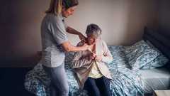 Eine Frau hilft einer pflegebedürftigen Person beim Anziehen, symbolisch für das Thema Pflegeversicherung und Angehörige.