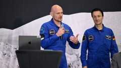 Two men stand next to a podium wearing blue space suits
