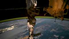 a green glow floats above earth in the background as a cylindrical space station module dominates the foreground