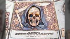 a plaque with a human skull dressed as a grim reaper with text that reads "the black death. the population of monmouth and the surrounding areas was decimated by the great pestilence in 1349 and again in 1369".