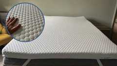 The Helix Premium Mattress Topper with GlacioTex in a tester's bedroom. On the top left foreground, there is a circular frame containing a close-up image of a hand feeling the GlacioTex cover.