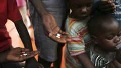 a group of Ugandan adults and children stand with HIV medication in their hands