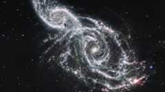 A deep space image showing the white gas and stars forming two spiral galaxies next to each other, stretching from the bottom right to top left of the image.