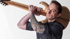 Composer Mick Gordon looking at camera while holding a guitar over his shoulder like a weapon.