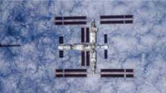a large T-shaped space station is seen from above with Earth below it