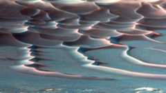 A false color image shows red sand dunes streaking across a blue surface
