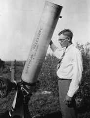 a young man stands next to a large Newtonian telescope.