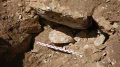 a piece of human skull sits at the bottom of two ancient walls at a corner