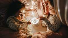 Two children in bed placing their finger on a star projector