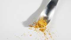 A metal spoon holds a yellow powder over a white surface