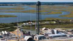 A zoomed out image of a the Rocket Lab launch complex, with a tall black water tower overlooking several buildings next to a wetland.
