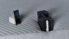 A close up of the 25kg weight balanced on the foot of the Siena Mattress for an edge support test, taking place in our sleep studio. There's a tap measure on the end of the weight and a red line, generated by a laser out of shot, indicates that the weight has sank roughly 3.6 inches into the mattress. To the left, a phone with a stopwatch indicates the test has been going on for 3 minutes 10 seconds.