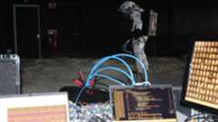A person wearing a white suit stands behind a desk with various wires and computers on it