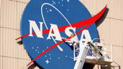 a person stands on a ladder and reaches towards a large nasa logo pasted on the outside of a building