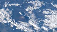 the snow-capped peak of a mountain is seen from far above the clouds in a photo taken by an astronaut on a space station.