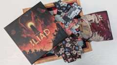 Iliad box, tiles, bag, and board on a white wooden surface