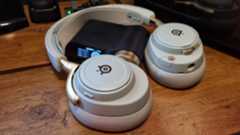 The SteelSeries Arctis Nova Elite gaming headset over its included DAC, in "sage gold" trim