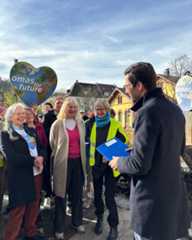 Dieser Alternativtext wurde KI-generiert: Eine Gruppe von Menschen steht und geht auf einer Straße. Sie halten Schilder mit Aufschriften, darunter eine Weltkugel.