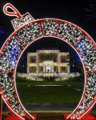 Dieser Alternativtext wurde KI-generiert: Ein großer, leuchtender Weihnachtsschmuck in Form eines Reifens umrahmt ein beleuchtetes Gebäude. Viele Lichter erhellen die Szene in der Nacht.