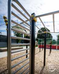 Dieser Alternativtext wurde KI-generiert: Eine Nahaufnahme von einer schwarzen Metallkonstruktion mit horizontalen Stangen im Freien. Im Hintergrund sind Bäume und ein Sportplatz zu sehen.