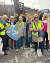 Dieser Alternativtext wurde KI-generiert: Eine Gruppe von Menschen steht zusammen und hält ein Schild mit einer Botschaft auf der Erde. Im Hintergrund ist eine Baustelle zu sehen.