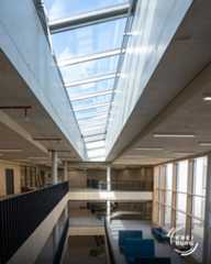 Dieser Alternativtext wurde KI-generiert: Ein Innenraum mit viel Tageslicht, der durch ein großes Oberlicht fällt. Architektonische Elemente aus Beton und Glas bestimmen das Bild.