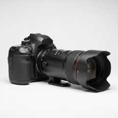 A digital SLR camera with a large lens attached, placed on a whilte background.