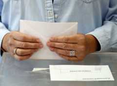 Una persona sostiene un sobre antes de introducirlo en la urna de un colegio electoral.