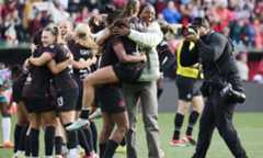 Soccer players in red and black uniforms celebrate on the field after winning a playoff game