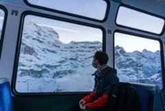 A young man travelling through the Swiss Alps by train during pandemic times. A young man travelling through the Swiss Alps by train during pandemic times.