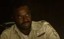 A man sits in the dark, looking serious.